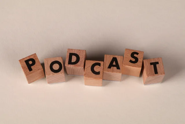 Wooden blocks spelling 'PODCAST' on a neutral background, symbolizing audio content creation. Measuring response from podcast promo codes