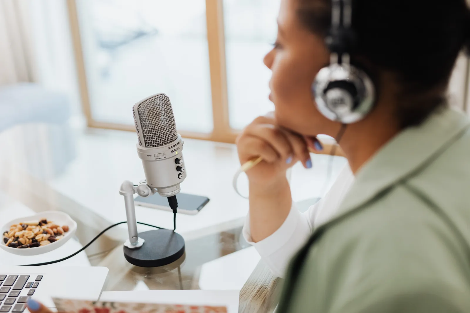 Woman using laptop and microphone for podcasting at home.