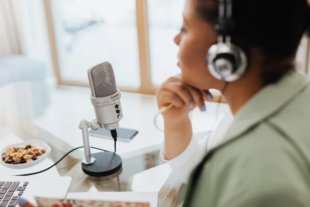 Woman using laptop and microphone for podcasting at home. Podcast ad frequency and reach