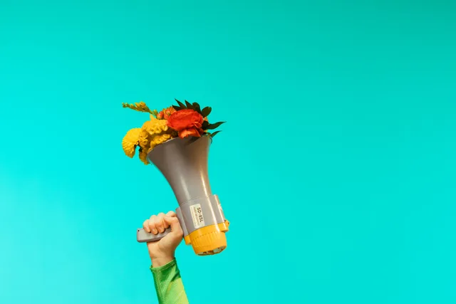 A creative composition featuring a hand holding a megaphone filled with vibrant flowers against a teal backdrop. Podcast advertising for Australian brands